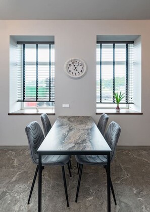 Un salón de conferencias con una mesa de mármol, cuatro sillas, un reloj y dos ventanas con persianas.