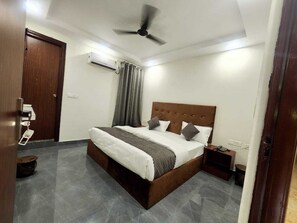 A bedroom with a bed, a ceiling fan, a nightstand, and a door. - Haridwar Harmony (Haridwar)