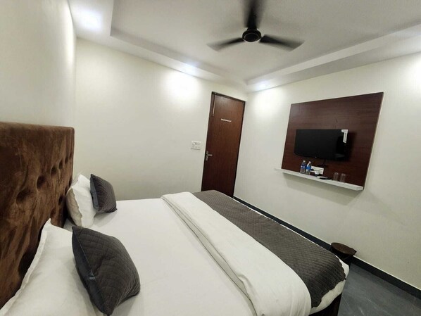 A hotel room with a bed, a ceiling fan, a TV mounted on the wall, and a door. - Haridwar Harmony (Haridwar)