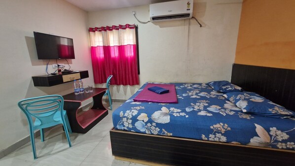 A bedroom with a bed, a desk with a chair, a TV, and an air conditioner. - Aditya Inn (Brahmapur)
