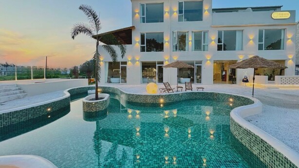 Un hotel moderno con piscina, sillas de descanso y una entrada bien iluminada.