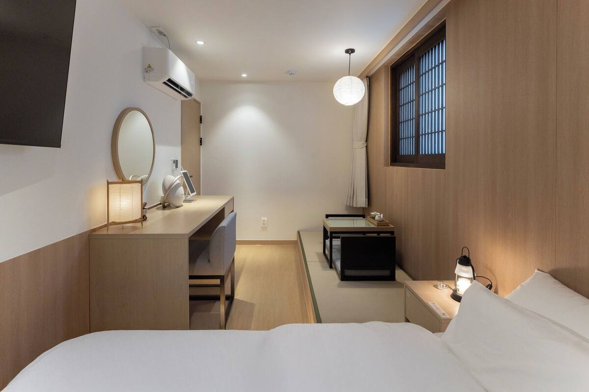 Camera d'albergo moderna con un letto, comodino, lampada e finestra con persiane.