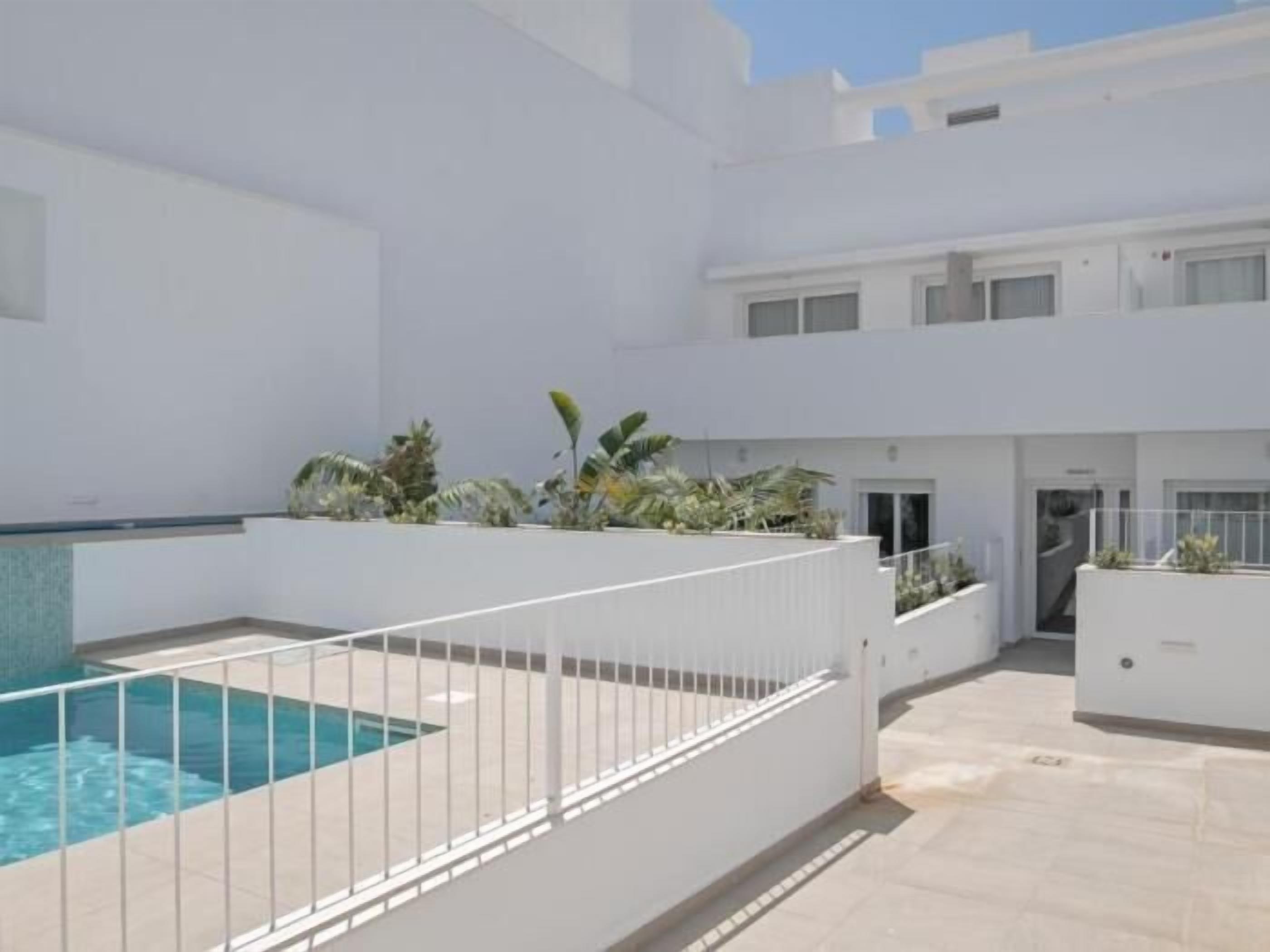 A modern building with a swimming pool, white walls, and a tiled patio area.