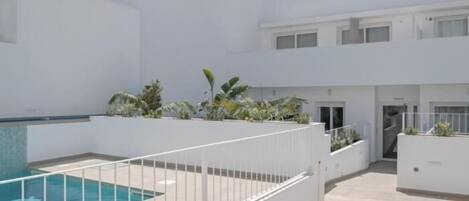 A modern building with a swimming pool, white walls, and a tiled patio area.