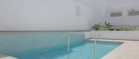 Una piscina con plataforma de baldosas y barandilla de metal.