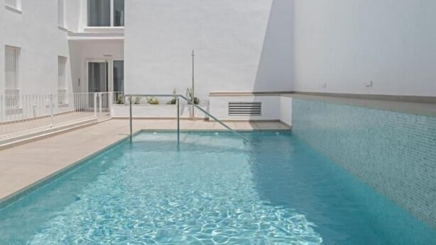 Una piscina con acqua cristallina, circondata da un edificio bianco con una porta e finestre.