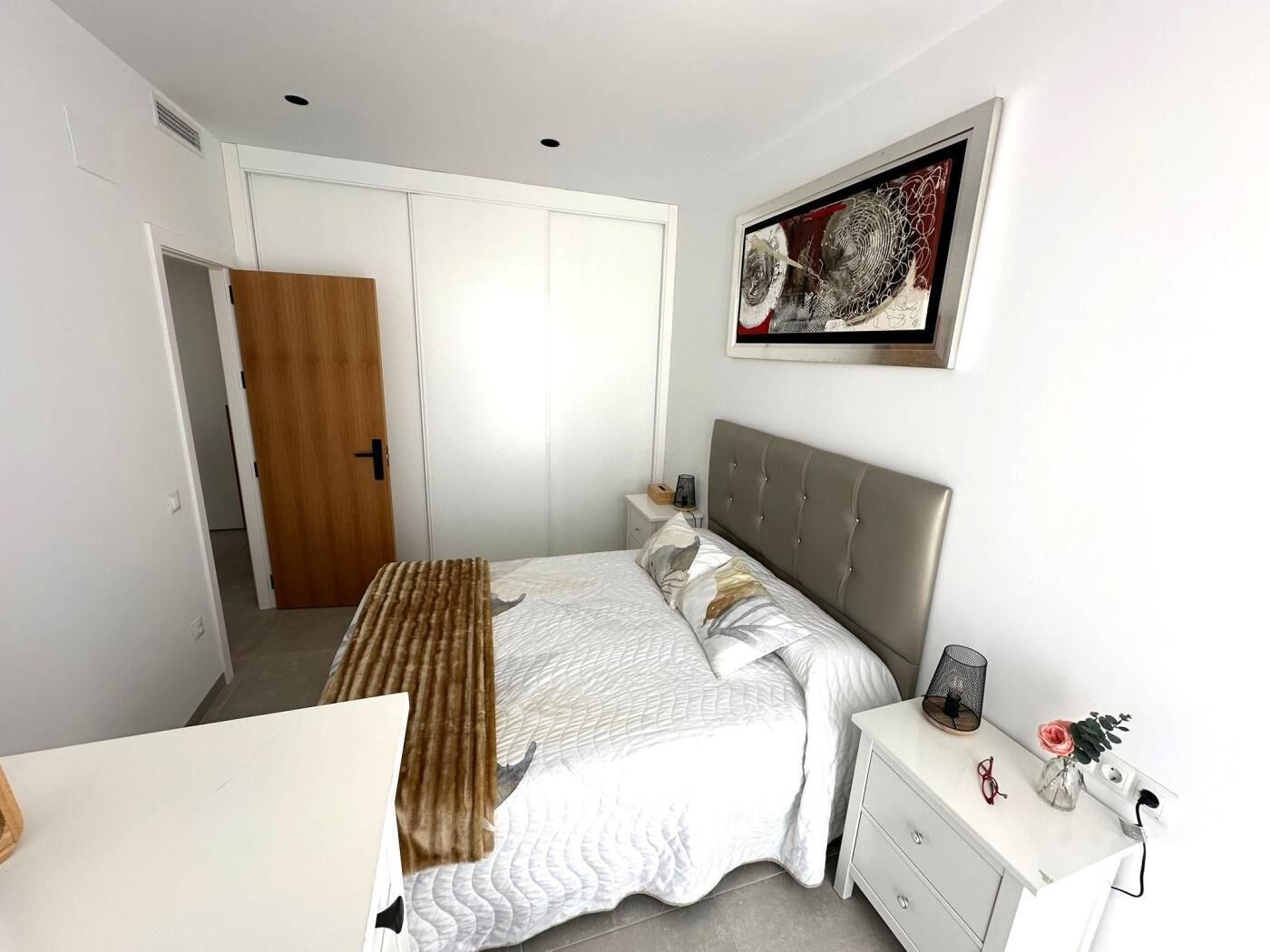 Quarto com cama, mesas de cabeceira, guarda-roupa e um quadro na parede.