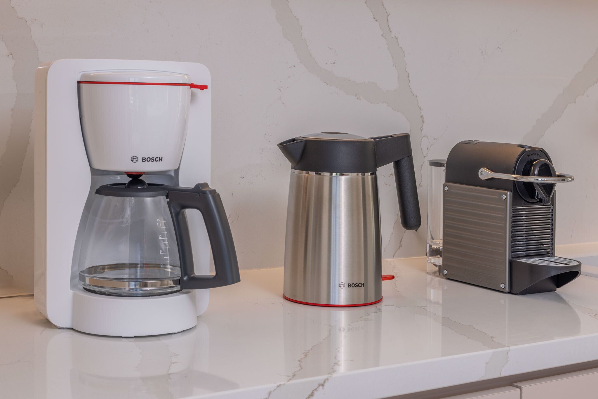 Eine Küche mit Kaffeemaschine, Wasserkocher und Toaster auf einer Marmorarbeitsplatte.