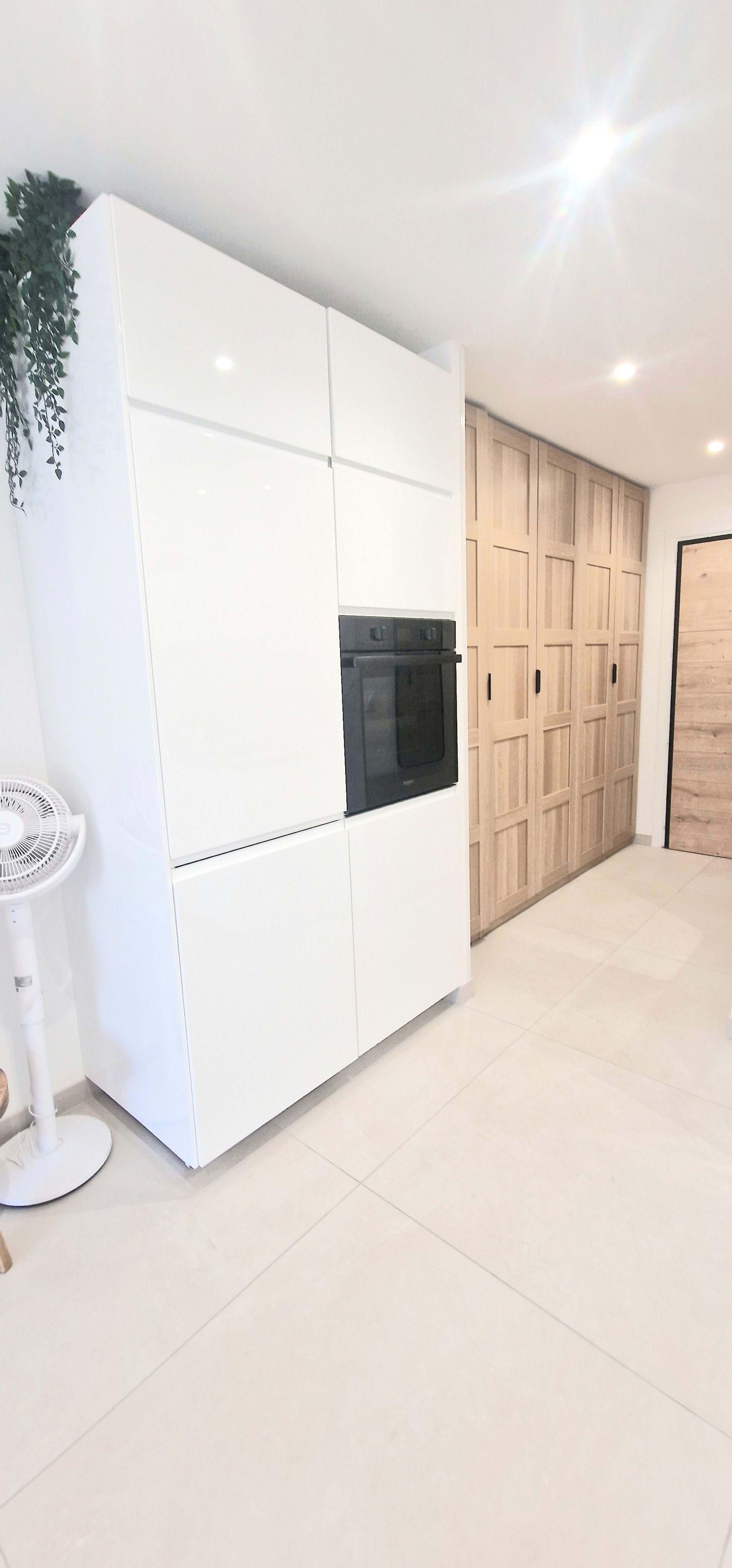 A modern kitchen with a built-in oven, white cabinetry, and a wooden door.
