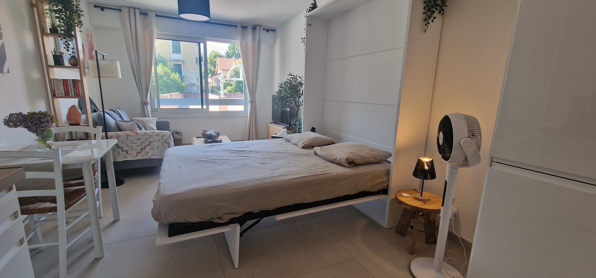 Een moderne slaapkamer met een bed, nachtkastje, lamp en een ventilator.