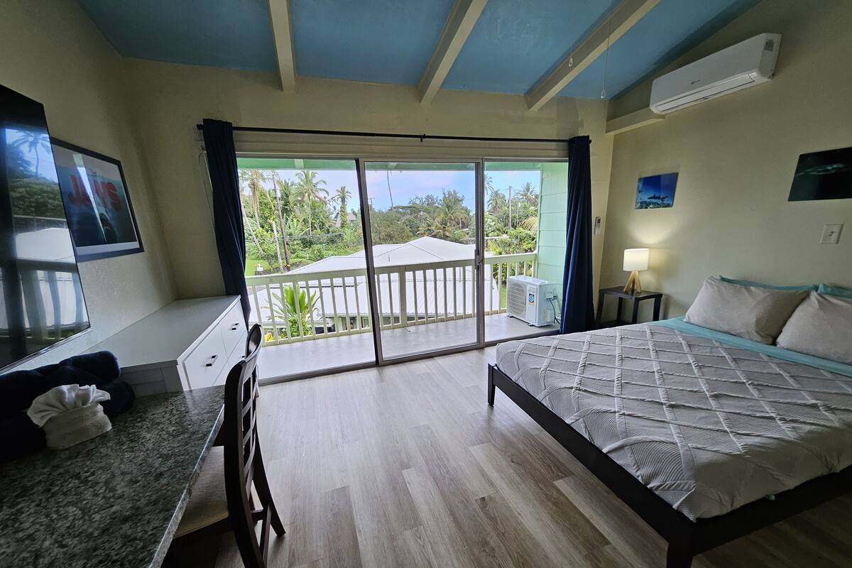 Quarto com cama, escrivaninha, cadeira, varanda e vista para palmeiras, além de ar condicionado.