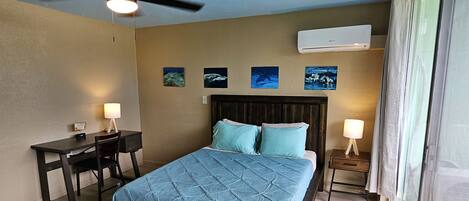 A bedroom with a bed, desk, chair, ceiling fan, and wall-mounted air conditioner.