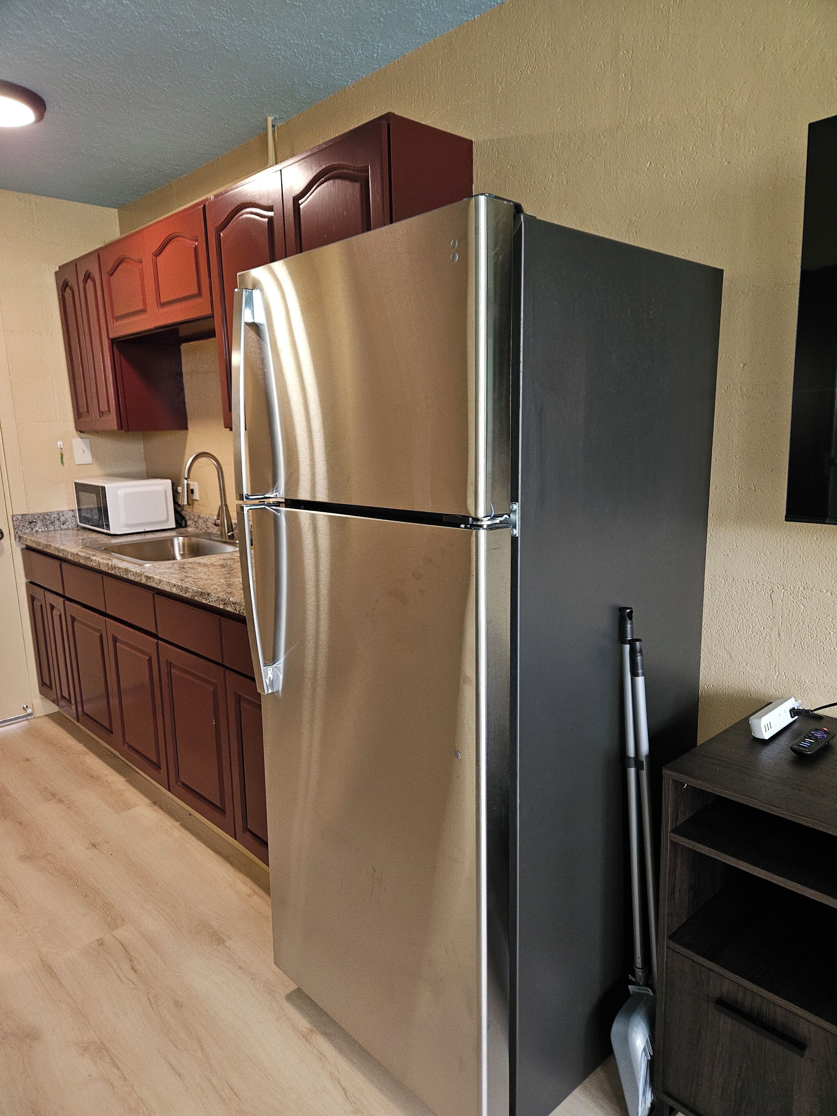 A kitchen with wooden cabinets, a stainless steel refrigerator, a microwave, and a sink.