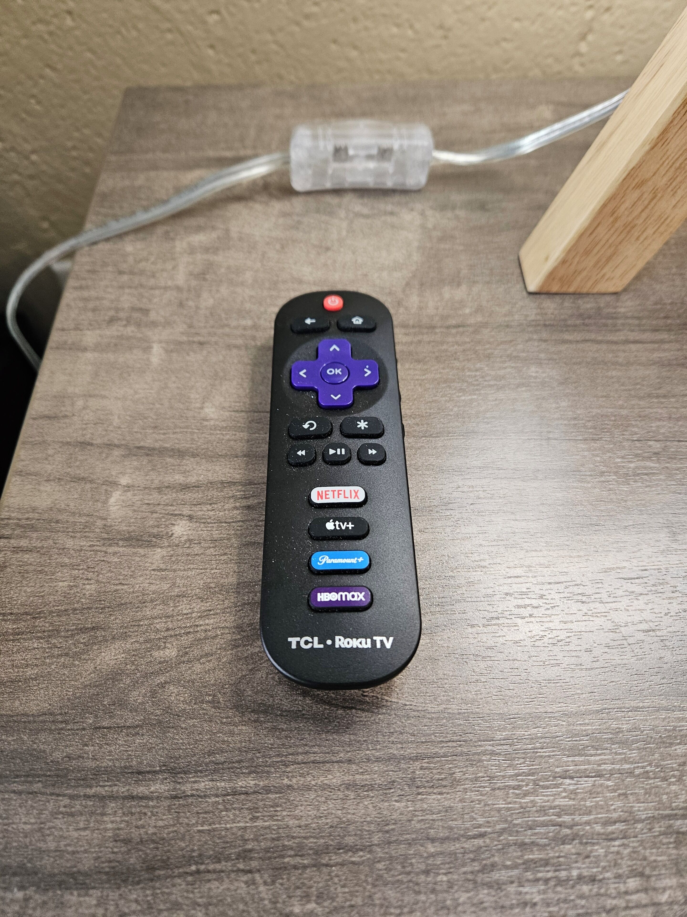 A black remote control with buttons for TCL Roku TV, Netflix, Apple TV+, Paramount+, HBO Max, and other functions.