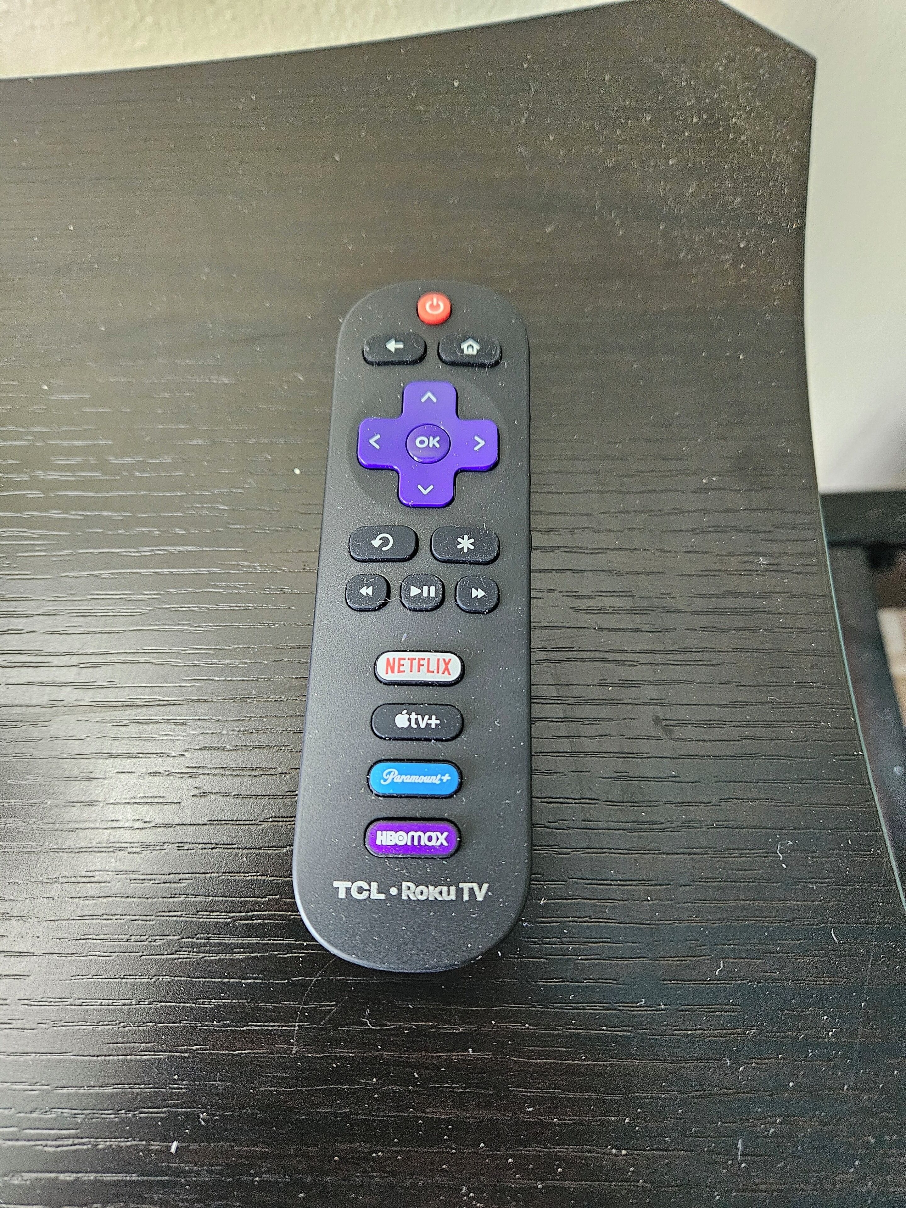 Une télécommande noire dotée de boutons pour Netflix, Apple TV+, Paramount+, HBO Max et les téléviseurs TCL Roku, posée sur une surface en bois.