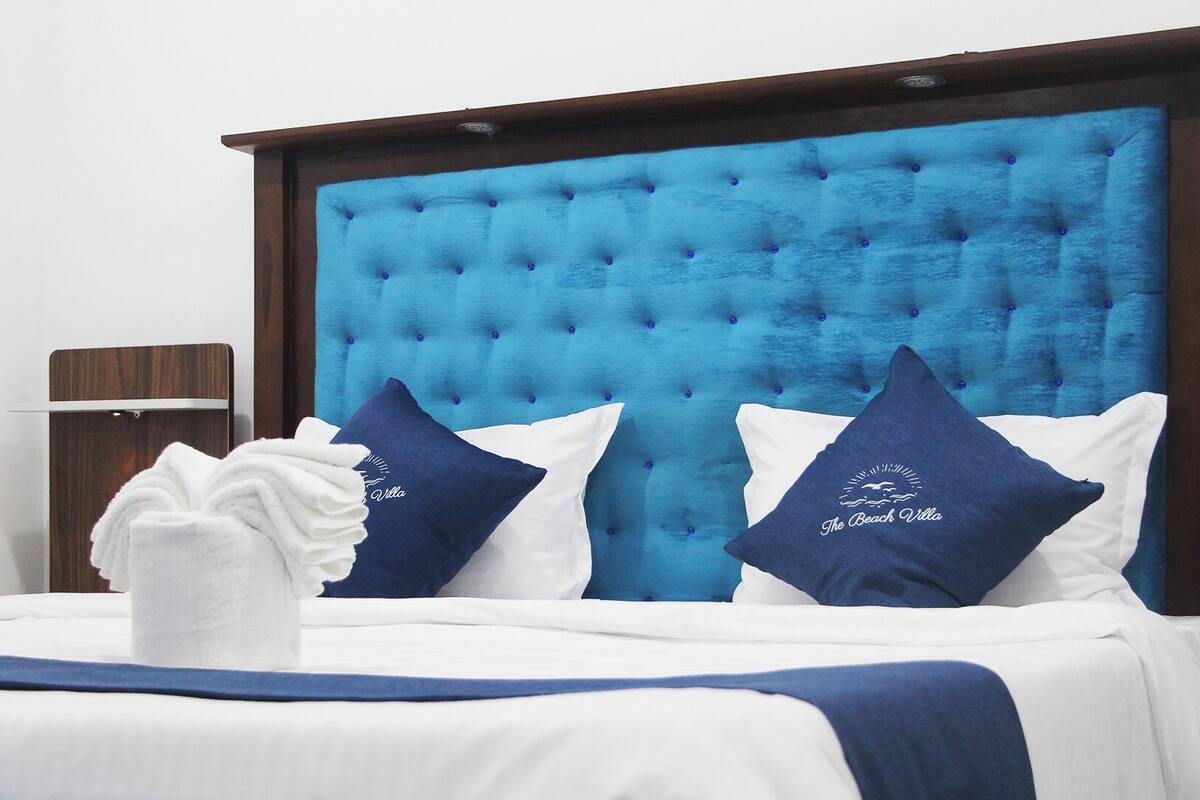 Ein Hotelzimmer mit hohem, gepolstertem Kopfteil, weißer Bettwäsche und zwei Zierkissen.