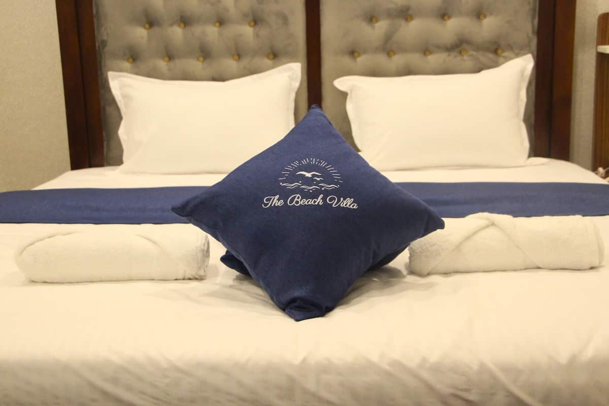 Ein Bett mit einem gesteppten Kopfteil, weißer Bettwäsche und einem Kopfkissen mit dem Logo "The Beach Villa".