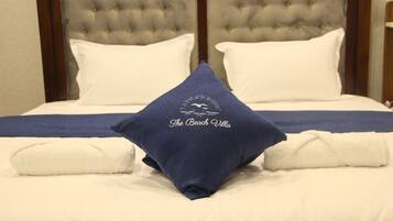 A bed with a tufted headboard, white bedding, and a pillow with "The Beach Villa" logo.