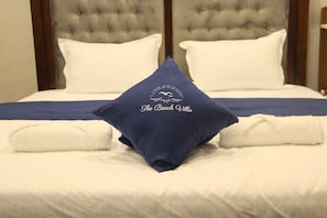 A bed with a tufted headboard, white bedding, and a pillow with "The Beach Villa" logo. - The Beach Villa  (Mount Lavinia)
