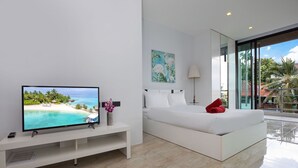 A modern bedroom with a large TV, a bed, a bedside table, and a window with a view of a beach and palm trees. - Lovely Pool Villa UTK B2 near Kata Beach (Karon)