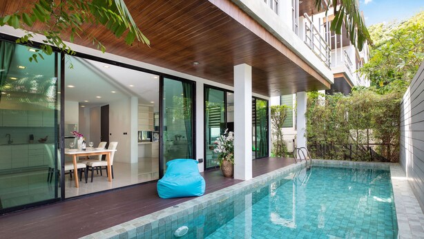 A modern outdoor pool area with a wooden deck, a blue bean bag, and a glass-enclosed dining area. - Lovely Pool Villa UTK B2 near Kata Beach (Karon)