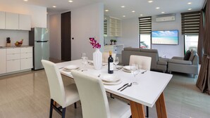 A modern kitchen with white cabinets, a stainless steel refrigerator, and a dining area with a white table set for four. - Lovely Pool Villa UTK B2 near Kata Beach (Karon)