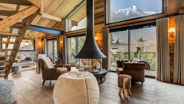 A cozy interior with a fireplace, wooden furniture, and a large window overlooking a mountain.