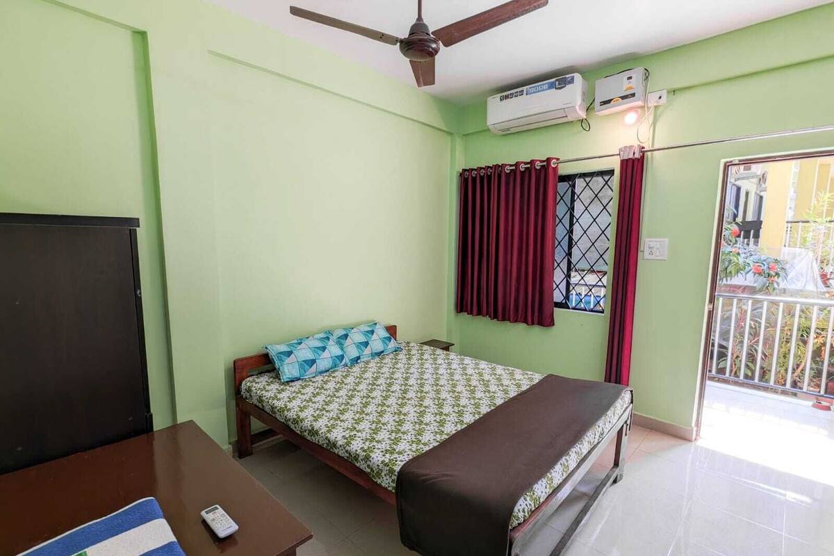 Une chambre avec un lit, un bureau, un ventilateur de plafond, un climatiseur et une fenêtre avec des rideaux.