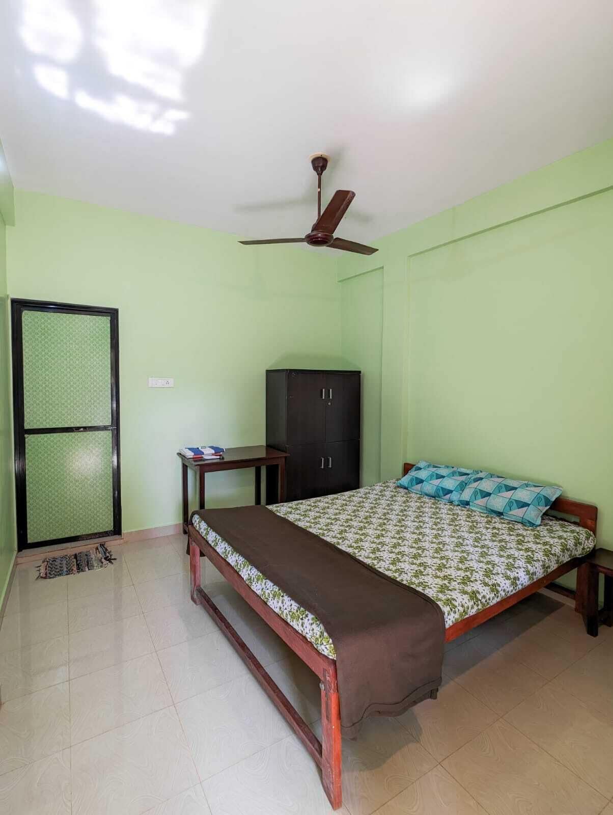 A bedroom with a bed, a desk, a wardrobe, and a ceiling fan.