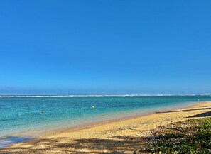 A beach with clear blue water, a sandy shore, and a clear sky.