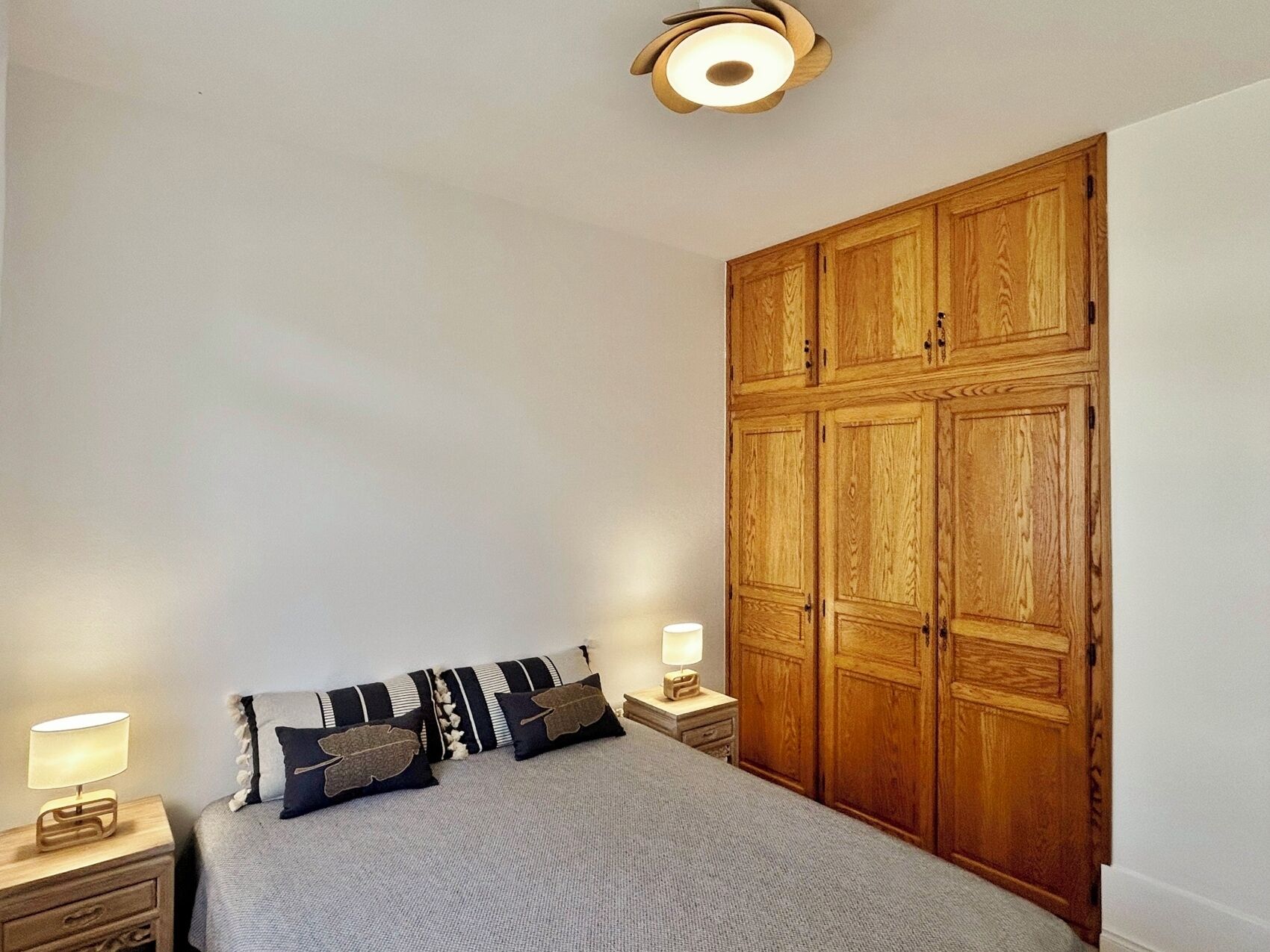 A bedroom with a bed, nightstands, a wooden wardrobe, and a ceiling light fixture.