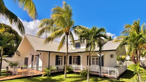 A two-story house with a white exterior, a covered porch, and a well-maintained lawn with palm trees. - *VILLA SOUS LES PALMES* - 170 m from the lagoon (Saint-Paul)