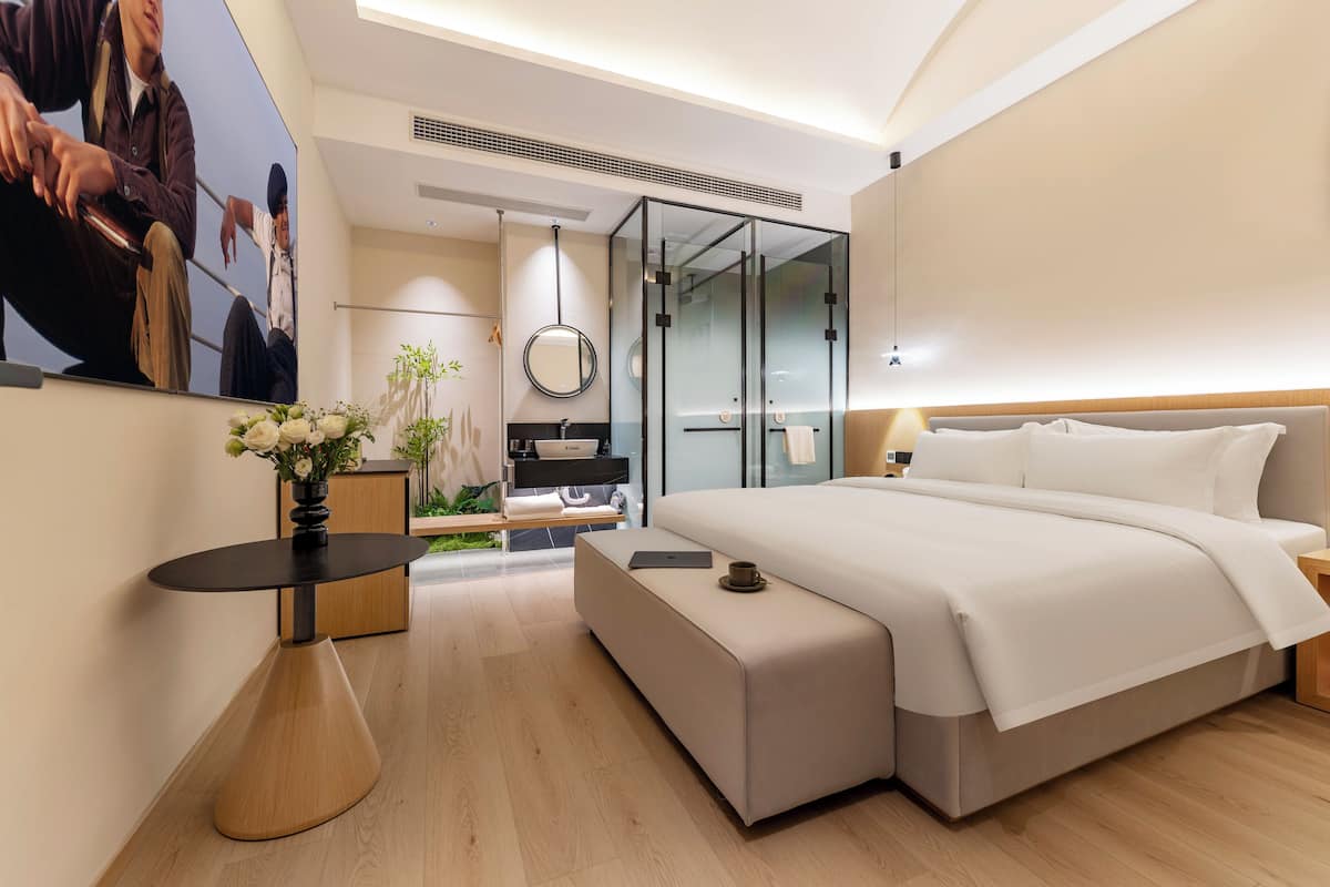 Ein modernes Schlafzimmer mit einem großen Bett, einem Nachttisch, einem Spiegel und einer kleinen Sitzecke.
