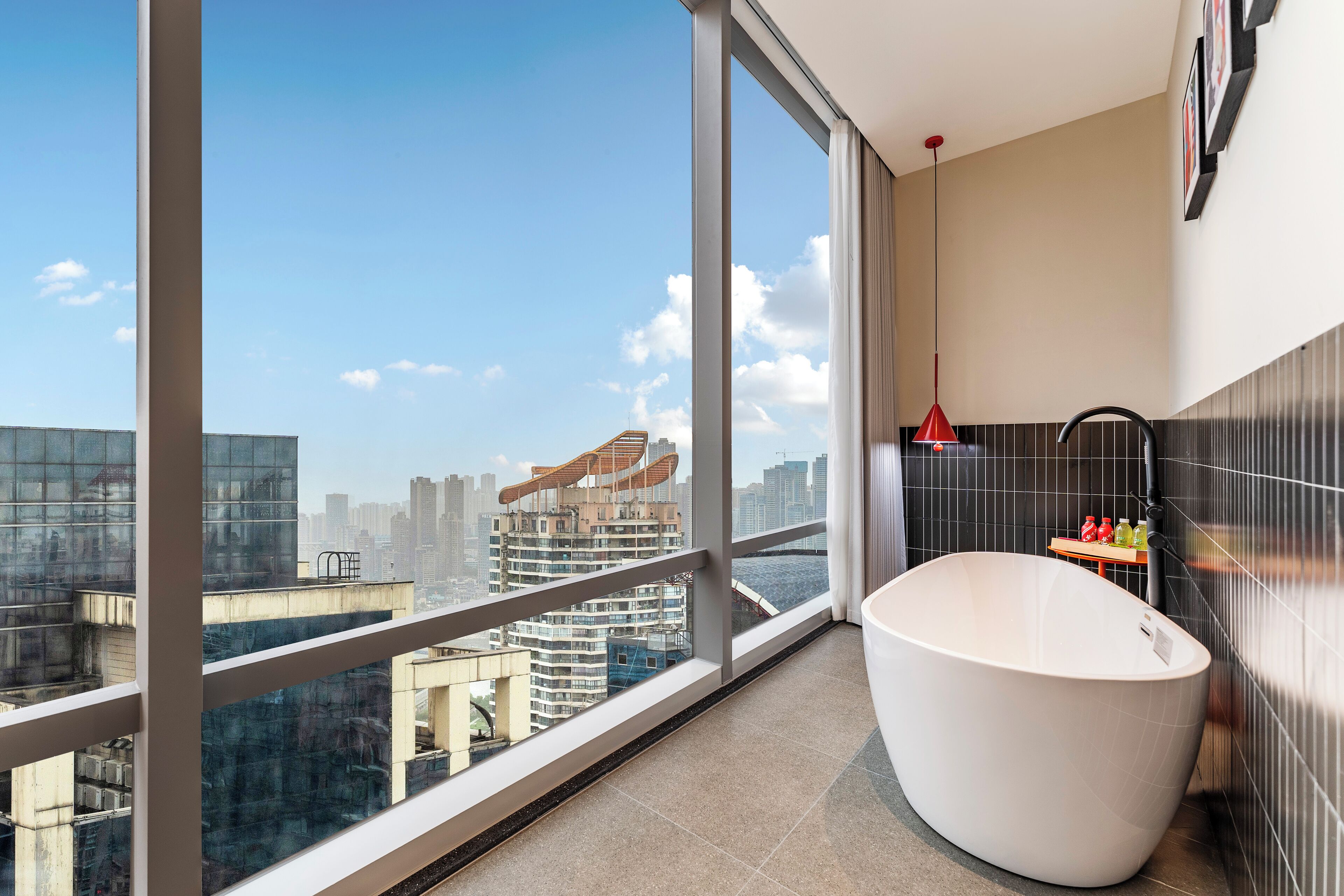 A modern bathroom with a large bathtub, a view of the cityscape, and a red pendant light.