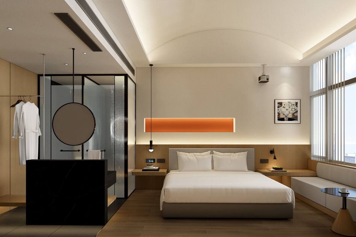 Ein modernes Hotelzimmer mit einem großen Bett, einem Schminktisch mit Spiegel, einem Nachttisch und Blick auf die Stadt durch große Fenster.