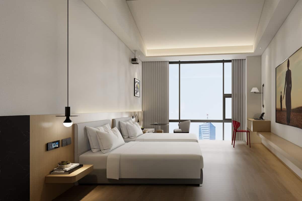 Ein modernes Hotelzimmer mit zwei Betten, einem Schreibtisch, einem Stuhl, einem großen Fenster mit Blick auf die Stadt und einem Bild an der Wand.