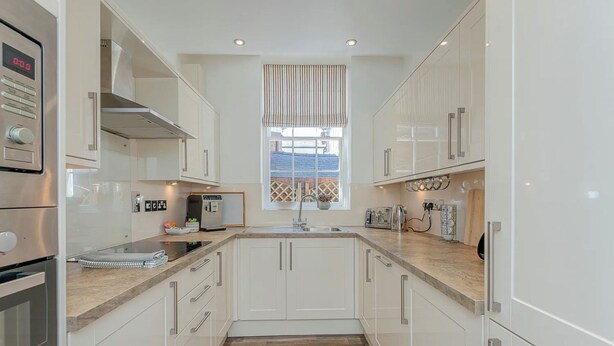 A modern kitchen with white cabinets, a built-in oven, and a window with vertical blinds. - Luxury Apartment, City Break, 4B City Cottage Central Chester (Chester)