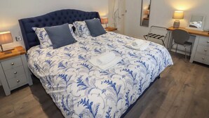 A neatly made bed with a floral bedspread, a bedside table with a lamp, a chair, and a desk with a lamp. - Luxury Apartment, City Break, 4B City Cottage Central Chester (Chester)