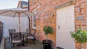 A brick house with a white door, a patio with a table and chairs, and a small potted plant. - Luxury Apartment, City Break, 4B City Cottage Central Chester (Chester)