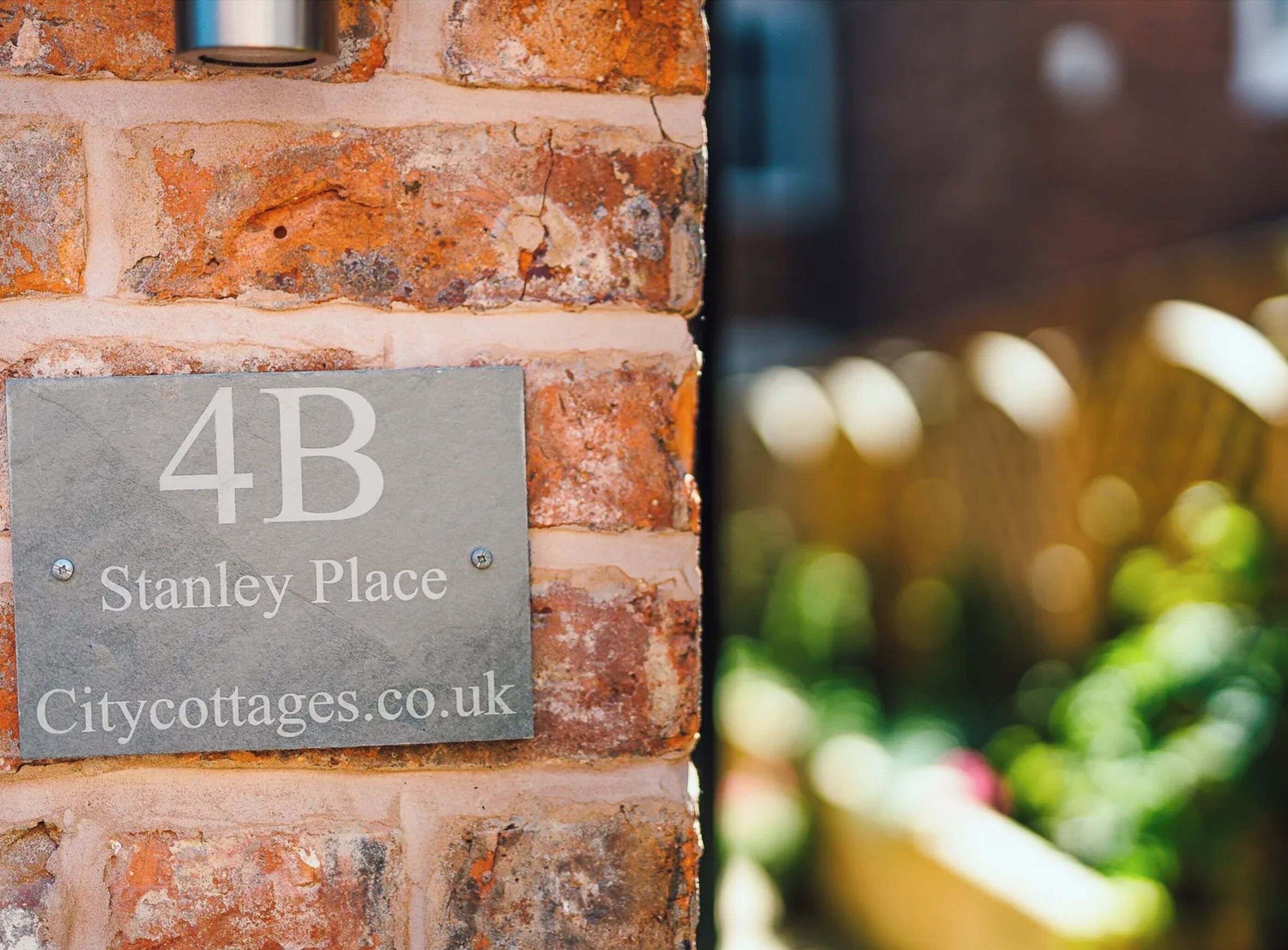 A brick wall with a sign reading "4B Stanley Place Citycottages.co.uk".
