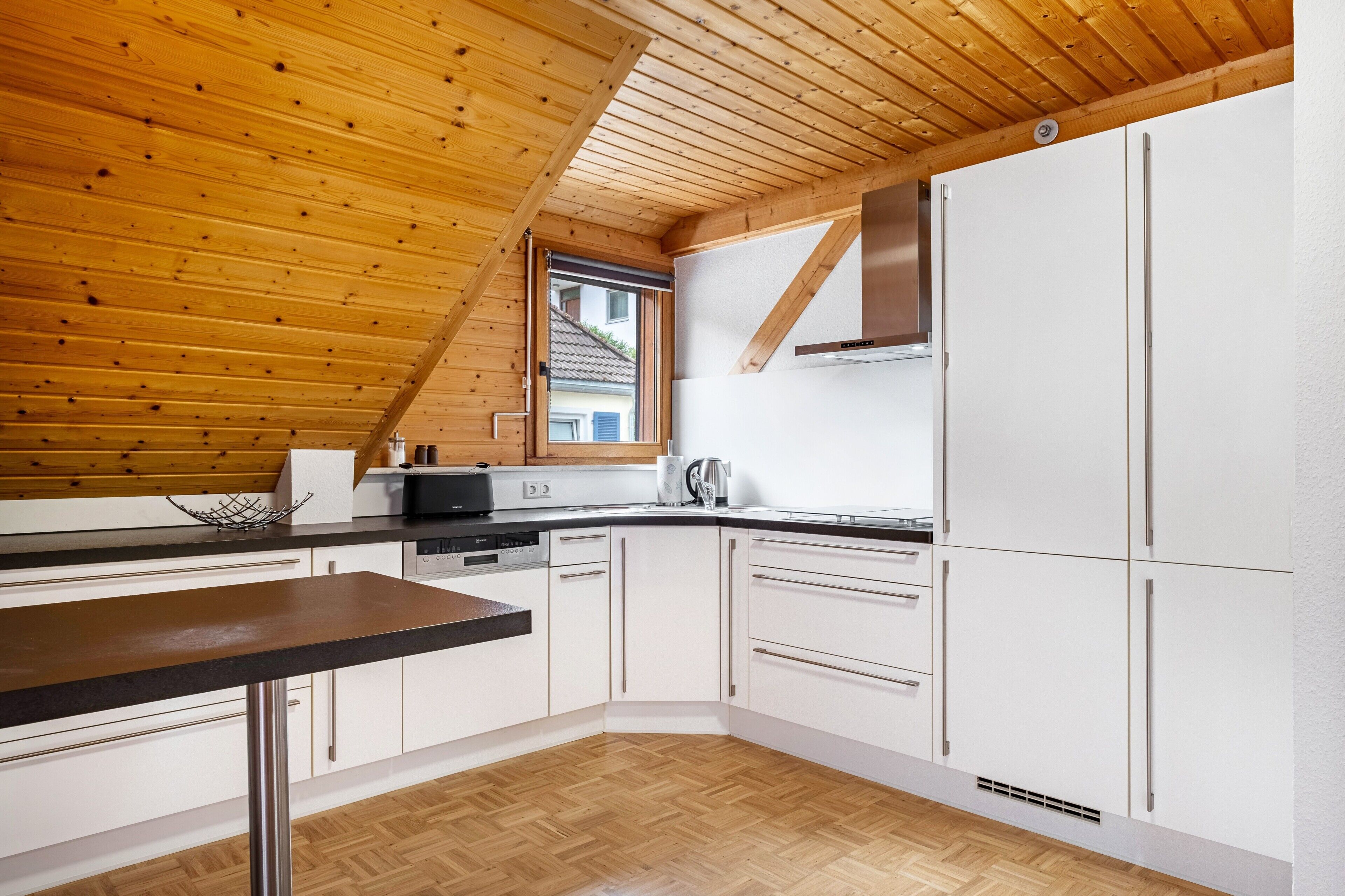 Eine Küche mit weißen Schränken, einer Holzbalkendecke und einem Fenster.