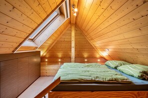 Un interior de madera con techo inclinado, una cama con ropa de cama verde y una ventana.