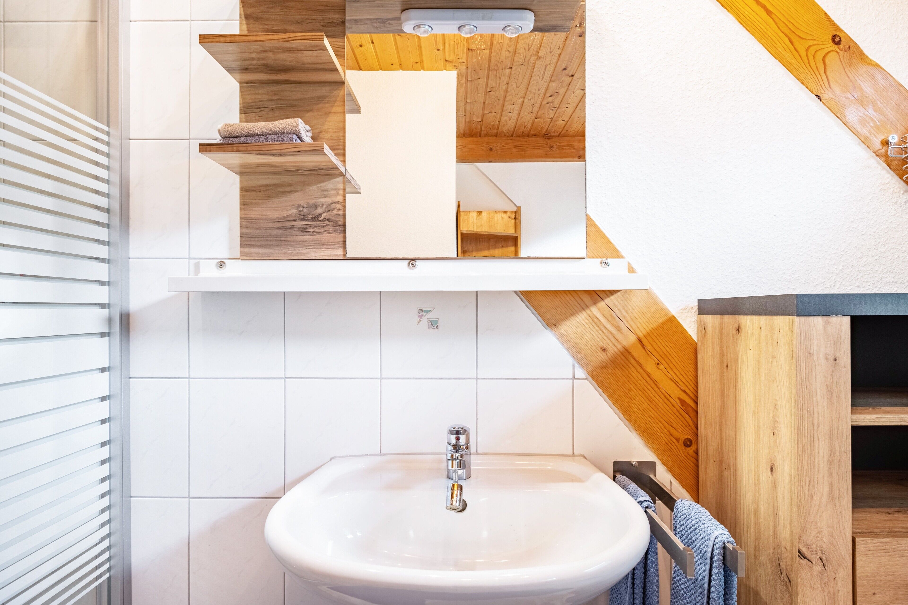 Une salle de bain avec un lavabo blanc, des étagères en bois et un plafond en bois.