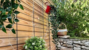 A wooden wall with a grid pattern, a yellow pot with green foliage, a red watering can, and a wicker basket. - Lodge Vitré with Nordic bath for an unusual night in Dijon (DIJON)