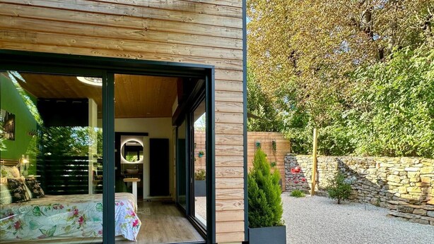 A modern house with a wooden exterior, a large glass door leading to a bedroom, and a gravel garden. - Lodge Vitré with Nordic bath for an unusual night in Dijon (DIJON)