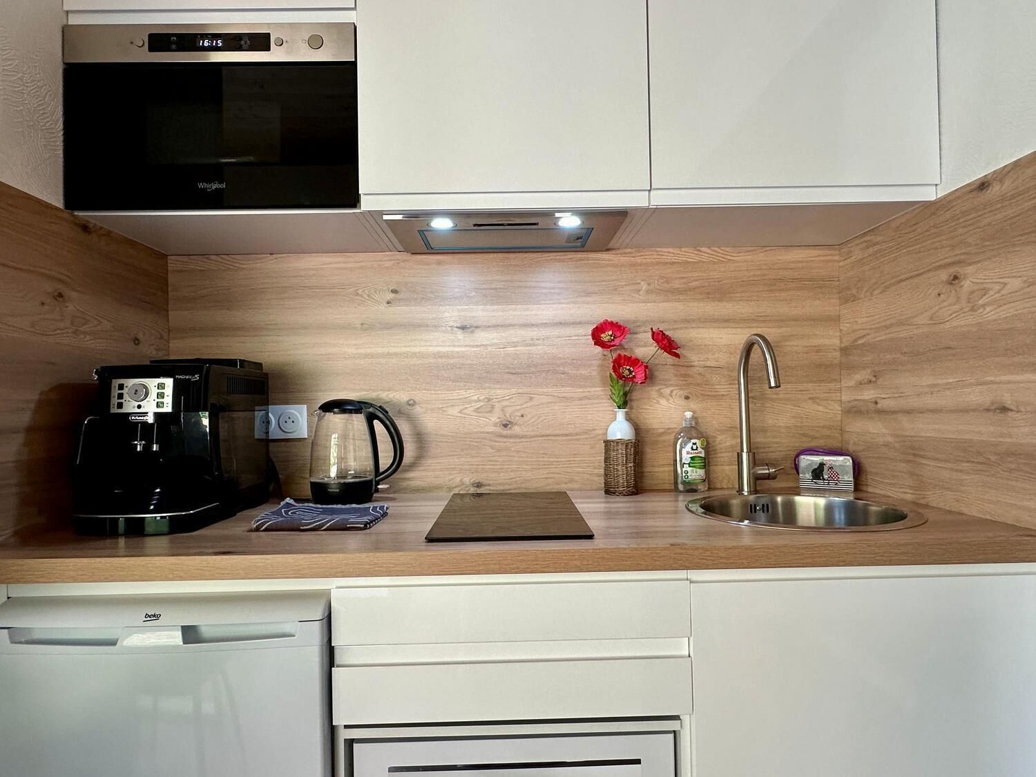 A compact kitchen with a built-in microwave, coffee maker, kettle, and a sink.