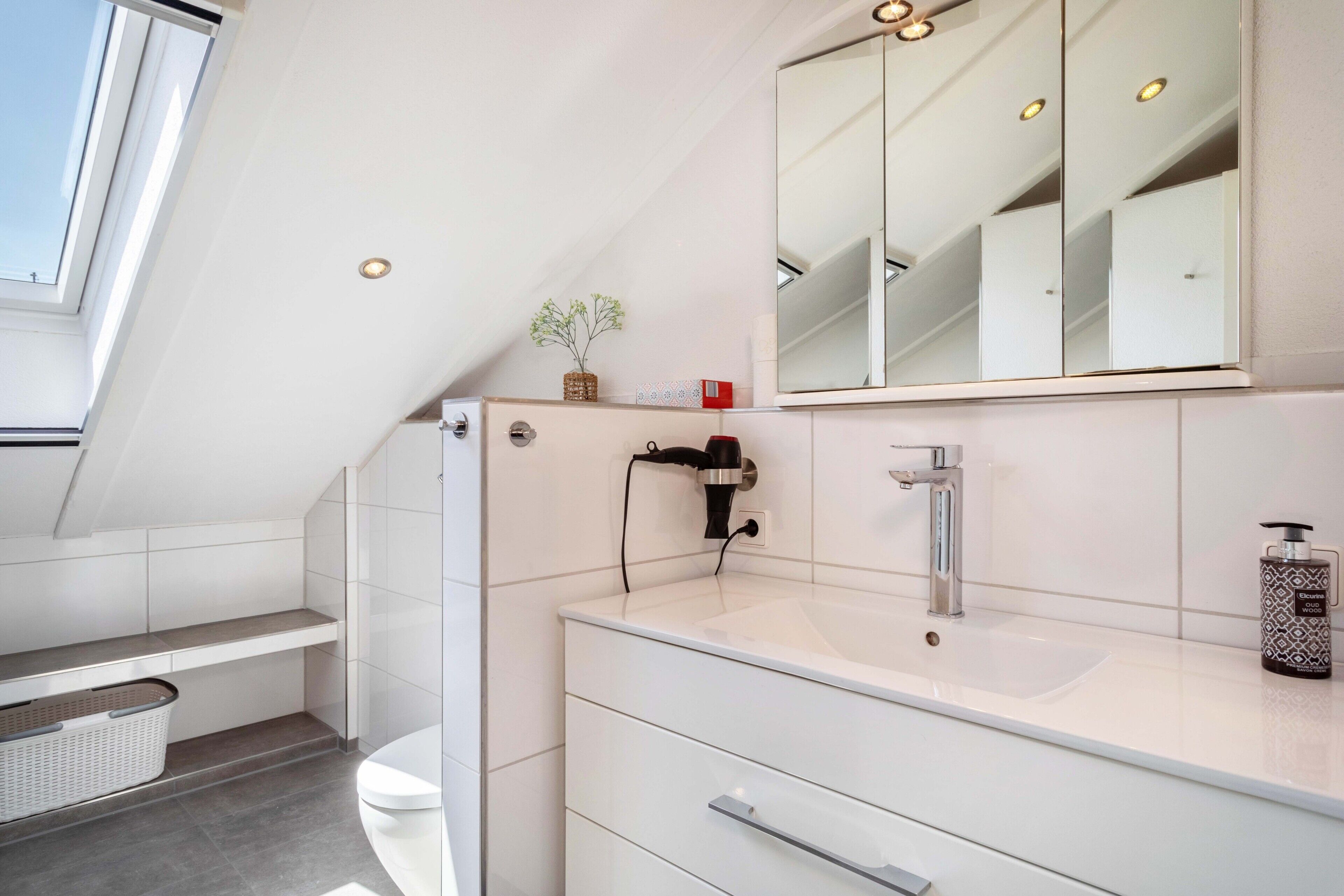 Et moderne badeværelse med ovenlys, stort spejl, håndvask og toilet.