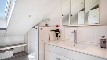 Et moderne badeværelse med ovenlys, stort spejl, håndvask og toilet.