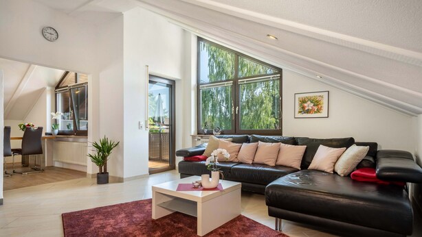 Un salon moderne avec un canapé en cuir noir, une table basse blanche et une grande fenêtre donnant sur la verdure.