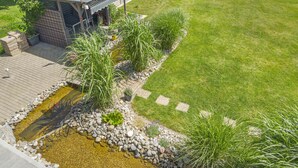 Un jardin aménagé avec un bassin, une terrasse en bois et un bâtiment doté d’un toit en métal.